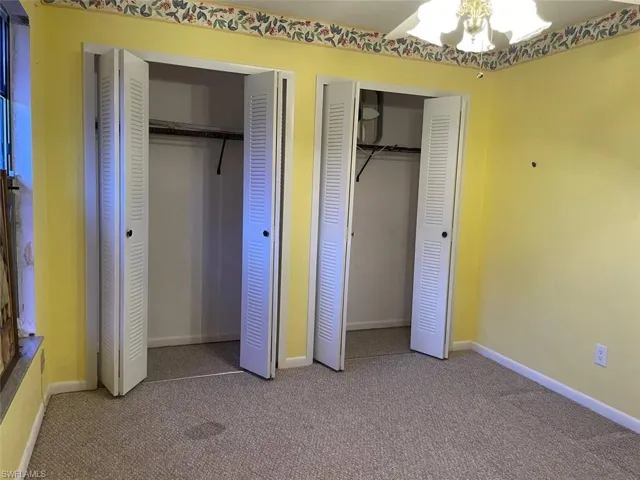 Carpeted interior space featuring two bi-fold louvered closet doors, wall-mounted light fixture, and decorative wallpaper border