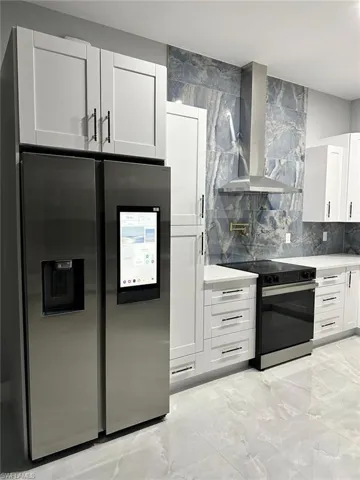 Kitchen featuring light countertops, electric range, decorative backsplash, stainless steel fridge, and exhaust hood