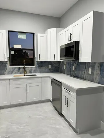 Kitchen featuring light quartz counters, decorative backsplash, appliances with stainless steel finishes, white cabinetry, and a sink