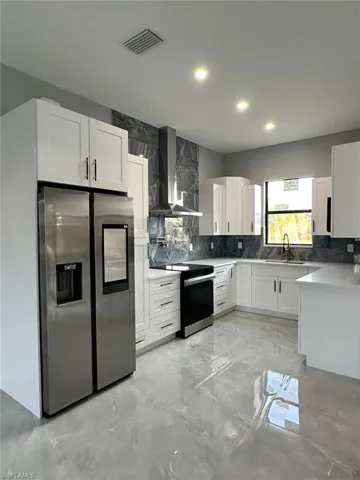Kitchen with visible vents, range with electric cooktop, wall chimney range hood, stainless steel fridge, and a sink