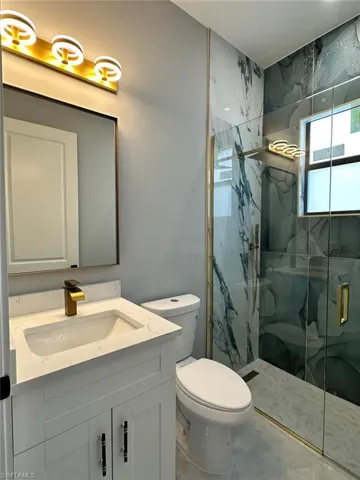 Bathroom featuring toilet, a marble finish shower, and vanity