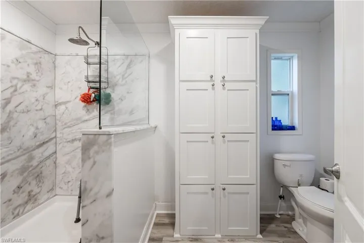 Shower enclosure with marble-patterned wall panels, glass partition, and a rain showerhead