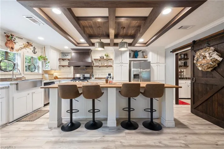 Kitchen featuring a large central island with seating, a farmhouse sink, stainless steel appliances, and wood-finish vinyl flooring
