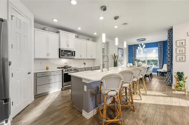 Kitchen with appliances with stainless steel finishes, pendant lighting, white cabinets, wood finish floors, and an island with sink