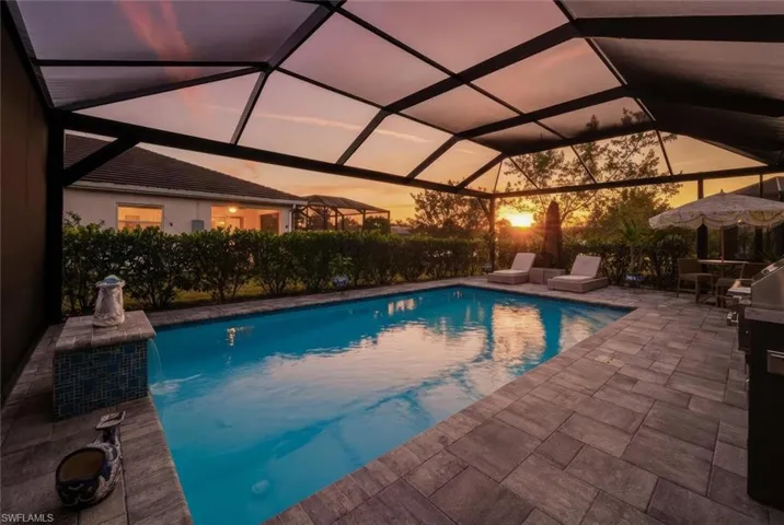 Pool at dusk with an outdoor pool, glass enclosure, and a patio