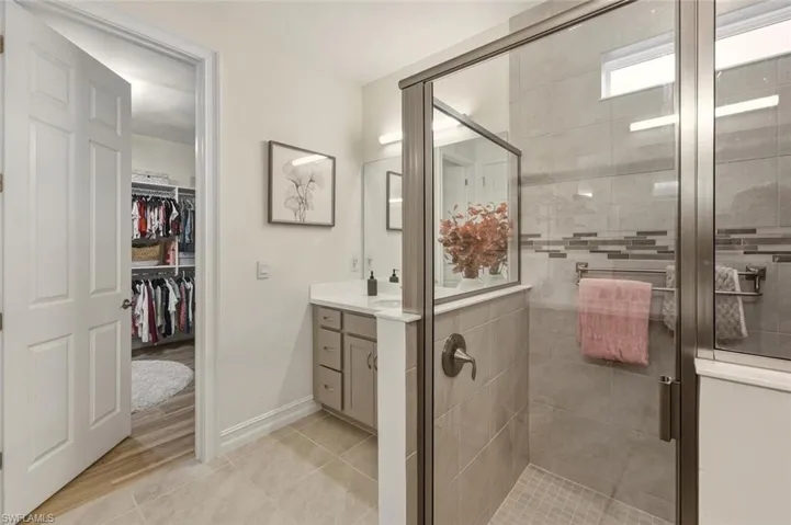 Full bathroom with vanity, a stall shower, a spacious closet, and light tile patterned floors