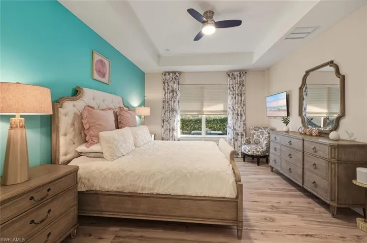 Bedroom with a raised ceiling, wood finished floors, and ceiling fan