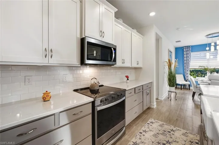 Kitchen featuring stainless steel appliances, white cabinets, wood finish floors, backsplash, and light stone countertops
