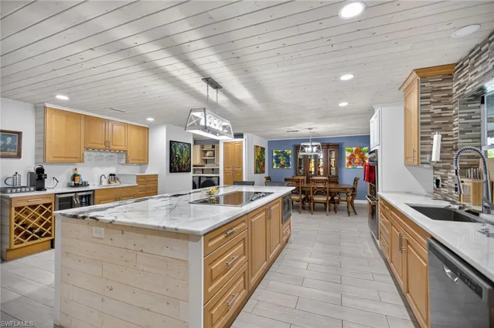 Kitchen featuring hanging light fixtures, decorative backsplash, light stone countertops, stainless steel appliances, and recessed lighting
