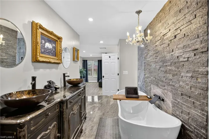 Bathroom with a chandelier, double vanity, a freestanding bath, and recessed lighting