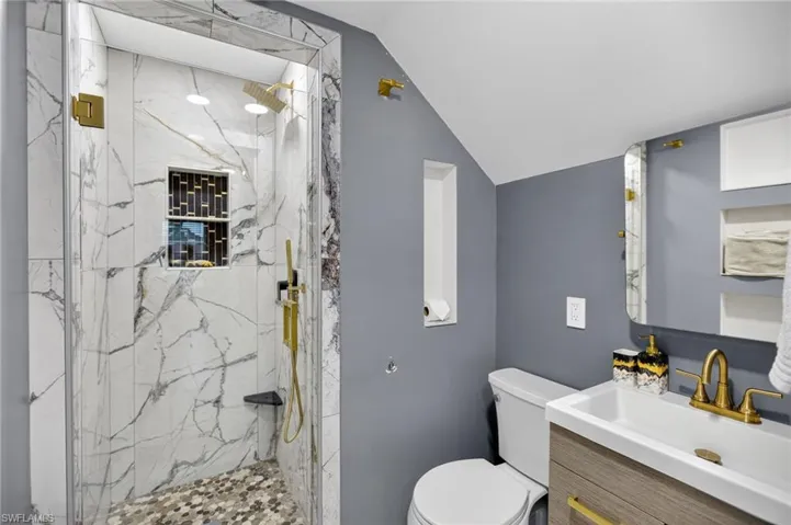 Full bathroom with vanity, a marble finish shower, and vaulted ceiling