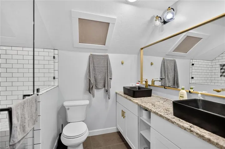 Bathroom with dark tile patterned floors, double vanity, vaulted ceiling, and tiled shower
