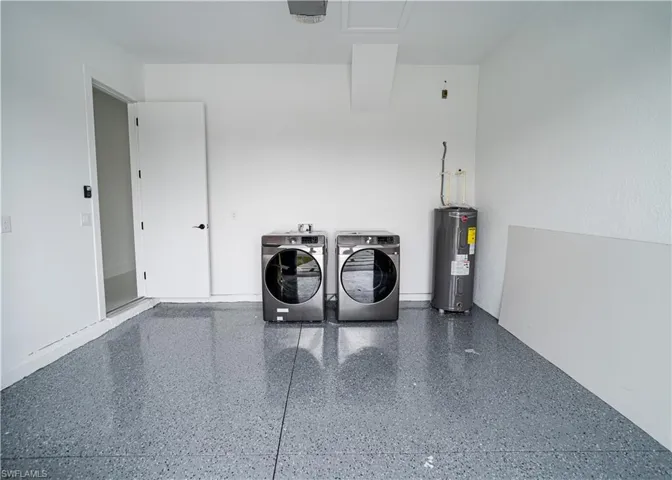 Washroom with washer and clothes dryer, water heater, and a garage
