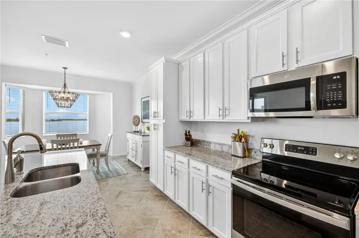 Kitchen with stainless steel appliances, light stone counters, white cabinets, ornamental molding, and pendant lighting