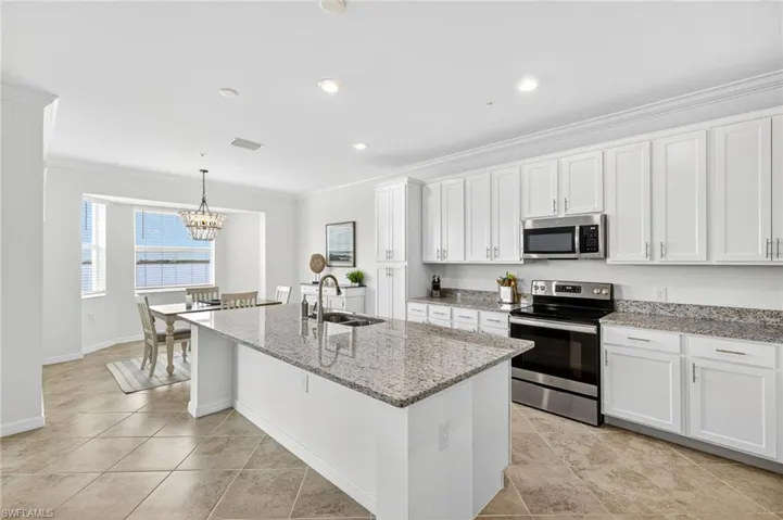 Kitchen with appliances with stainless steel finishes, white cabinetry, light stone counters, ornamental molding, and pendant lighting