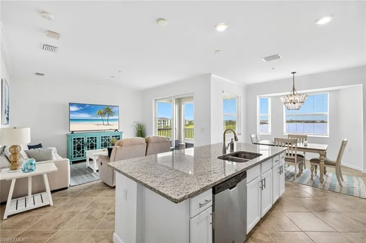 Kitchen featuring open floor plan, crown molding, light stone countertops, white cabinetry, and stainless steel dishwasher