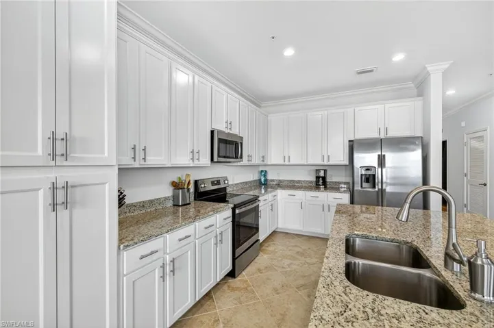 Kitchen featuring appliances with stainless steel finishes, white cabinetry, ornamental molding, light stone counters, and recessed lighting