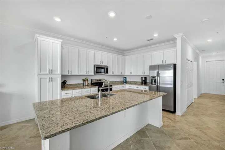 Kitchen featuring appliances with stainless steel finishes, white cabinets, light stone countertops, ornamental molding, and recessed lighting