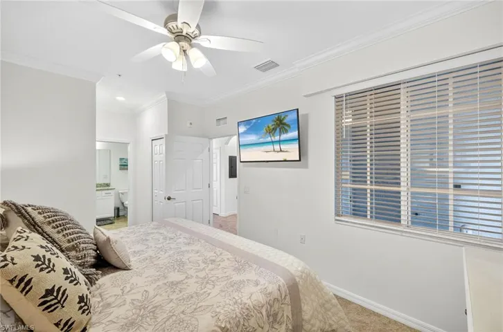 Carpeted bedroom featuring crown molding, connected bathroom, a ceiling fan, and a closet