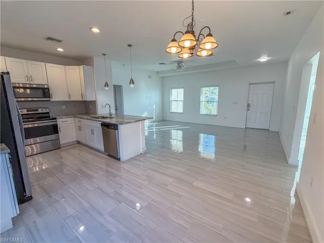Kitchen featuring a chandelier, stainless steel appliances, open floor plan, light stone countertops, and a peninsula