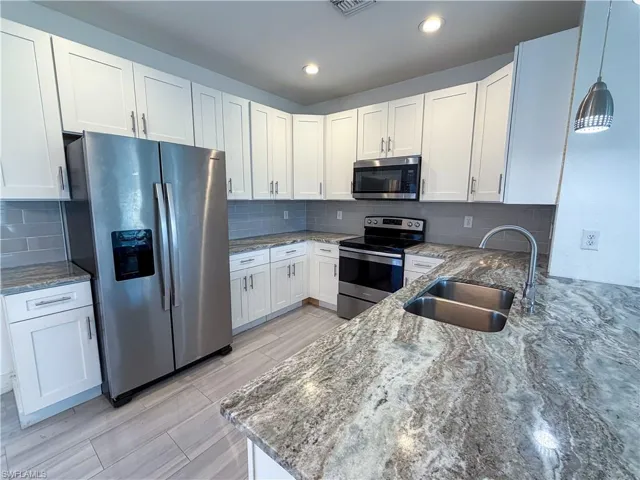 Kitchen with light stone counters, white cabinets, stainless steel appliances, and pendant lighting