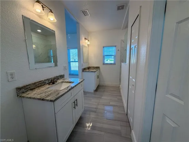 Bathroom with a marble finish shower, two vanities, and a textured wall