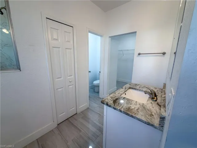 Full bathroom featuring vanity, a textured wall, and a walk in closet