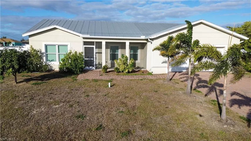 Ranch-style house featuring a metal roof, stucco siding, a sunroom, a front lawn, and a garage