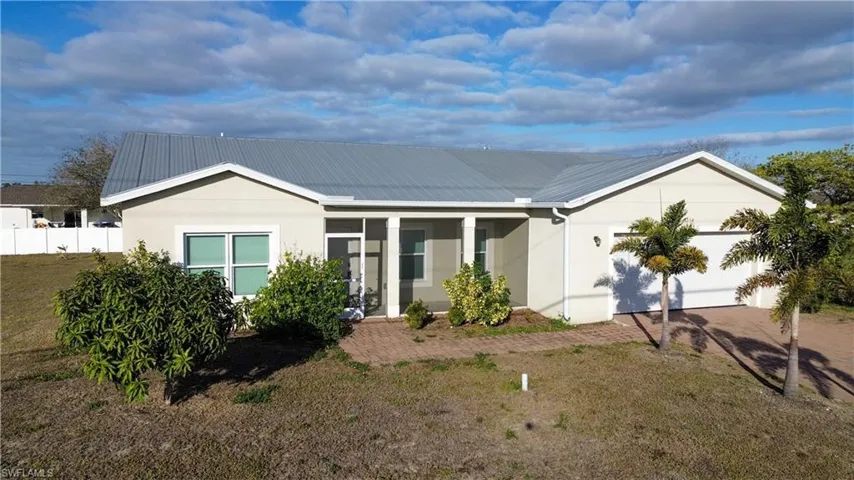 Single story home with a metal roof, a porch, an attached garage, stucco siding, and driveway