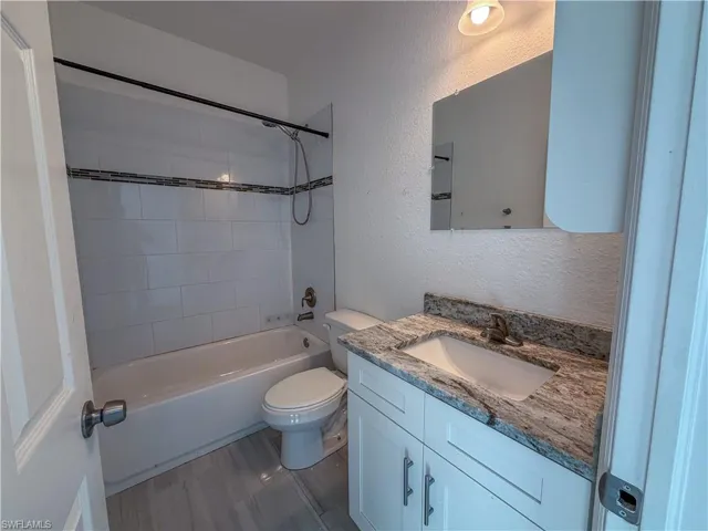 Full bath with a textured wall, vanity, and shower / tub combination