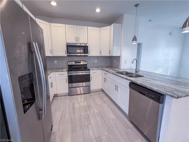 Kitchen with stainless steel appliances, white cabinets, light stone countertops, decorative backsplash, and a peninsula