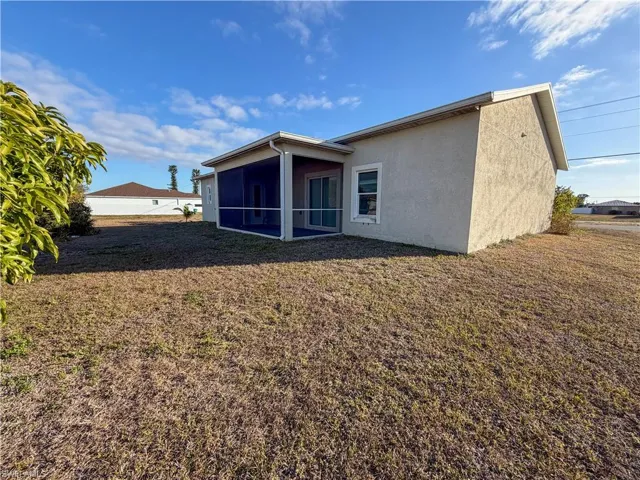 Rear view of property featuring a lawn, stucco siding, and a sunroom