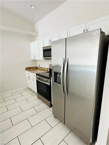 Kitchen with stainless steel appliances, white cabinets, dark stone counters, and light tile patterned floors