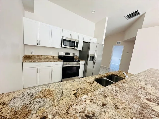 Kitchen with stainless steel appliances, light stone countertops, white cabinetry, and lofted ceiling