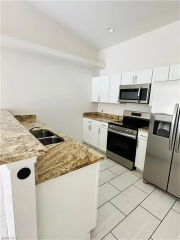 Kitchen featuring stainless steel appliances, white cabinetry, light stone countertops, light tile patterned flooring, and a peninsula