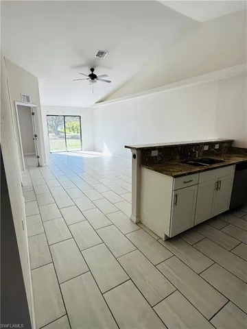 Kitchen featuring dark stone countertops, ceiling fan, vaulted ceiling, dishwasher, and open floor plan