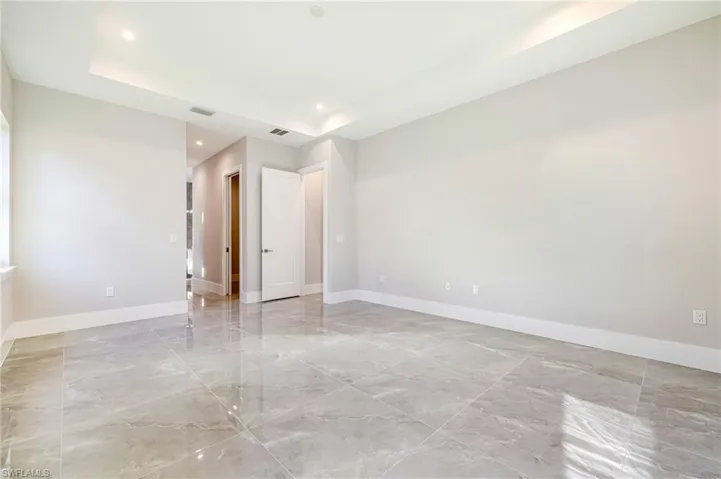 Empty room featuring a raised ceiling, light marble finish flooring, and recessed lighting