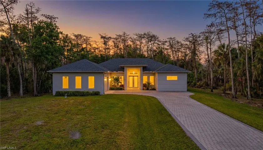Prairie-style house featuring a lawn, view of wooded area, driveway, and stucco siding