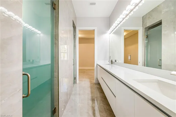 Bathroom with double vanity, a stall shower, and light marble finish flooring