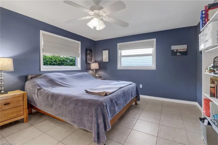 Tiled bedroom featuring ceiling fan and multiple windows