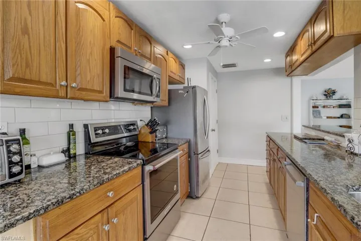 Kitchen featuring light tile patterned floors, ceiling fan, dark stone countertops, stainless steel appliances, and tasteful backsplash
