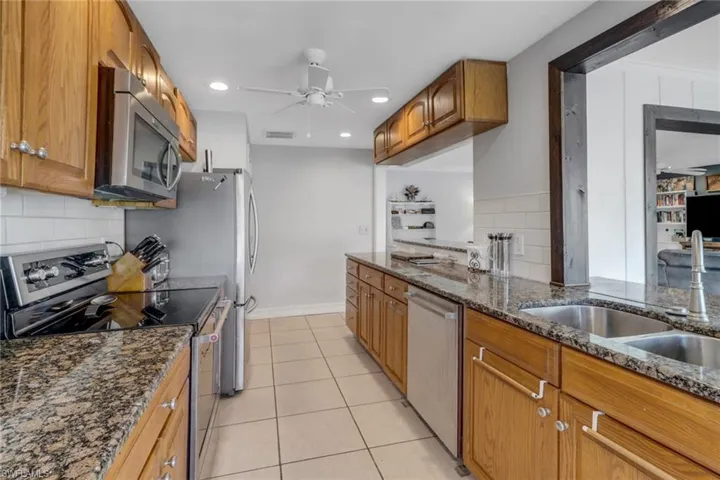 Kitchen with appliances with stainless steel finishes, light tile patterned floors, ceiling fan, and dark stone counters
