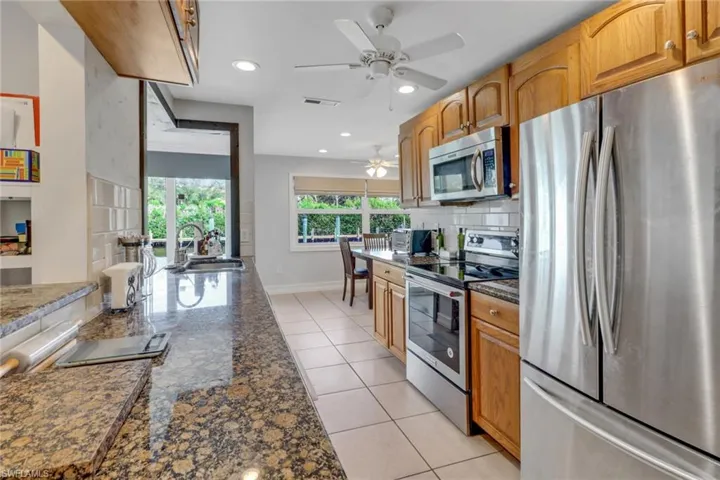 Kitchen with sink, decorative backsplash, dark stone counters, light tile patterned floors, and stainless steel appliances