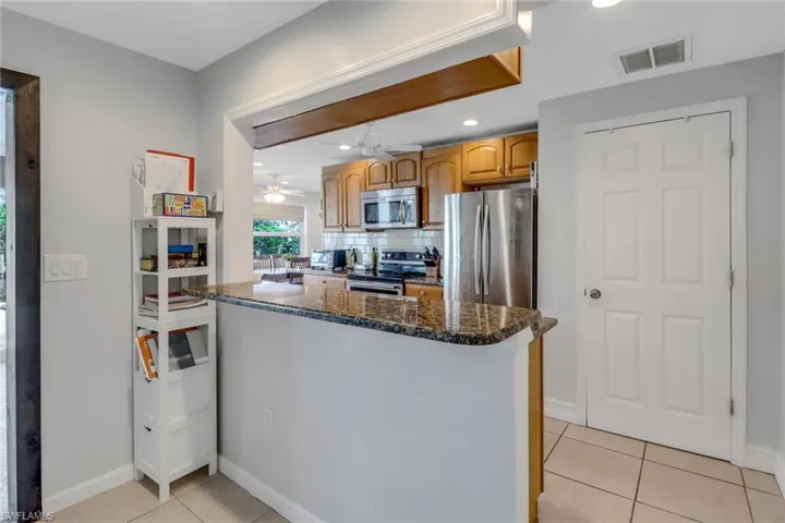 Kitchen with light tile patterned flooring, appliances with stainless steel finishes, decorative backsplash, and dark stone counters