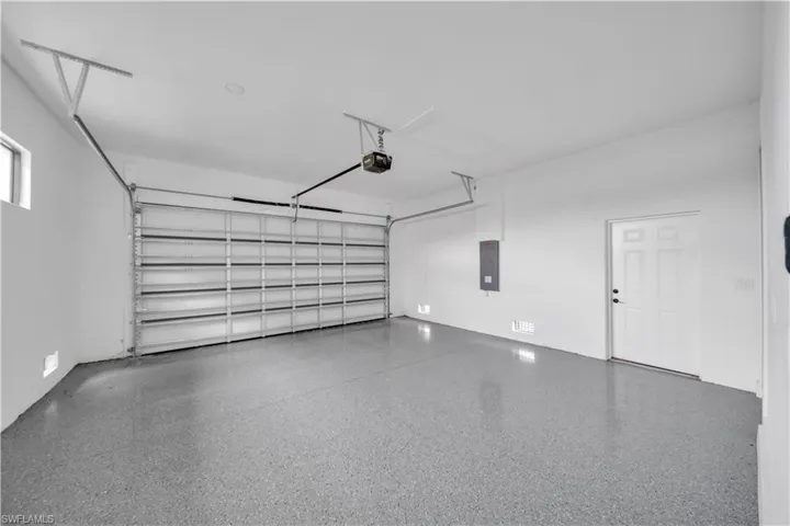 Spacious garage with epoxy flooring, automatic garage door opener, side entry door, and wall-mounted electrical panel