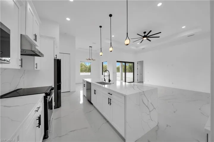 Open-concept kitchen featuring an expansive island with a waterfall countertop, white cabinetry with black hardware, and integrated stainless steel appliances