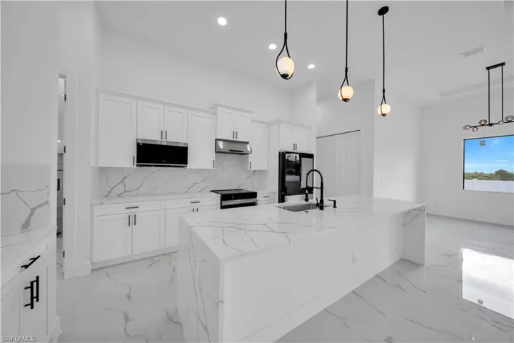 Modern kitchen featuring an expansive island with an undermount sink, white cabinetry, integrated stainless steel appliances, and matching countertops and backsplash