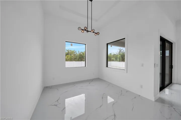 Vaulted ceiling with an attached light fixture, large windows with dark frames, white walls, and a sliding glass door