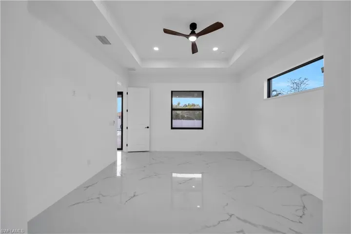Recessed ceiling with an integrated ceiling fan and lighting, two framed windows, and large format tile flooring