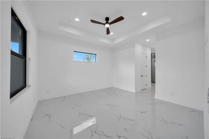 Spacious room featuring large format tile flooring, a tray ceiling with recessed lighting, an installed ceiling fan, and multiple windows